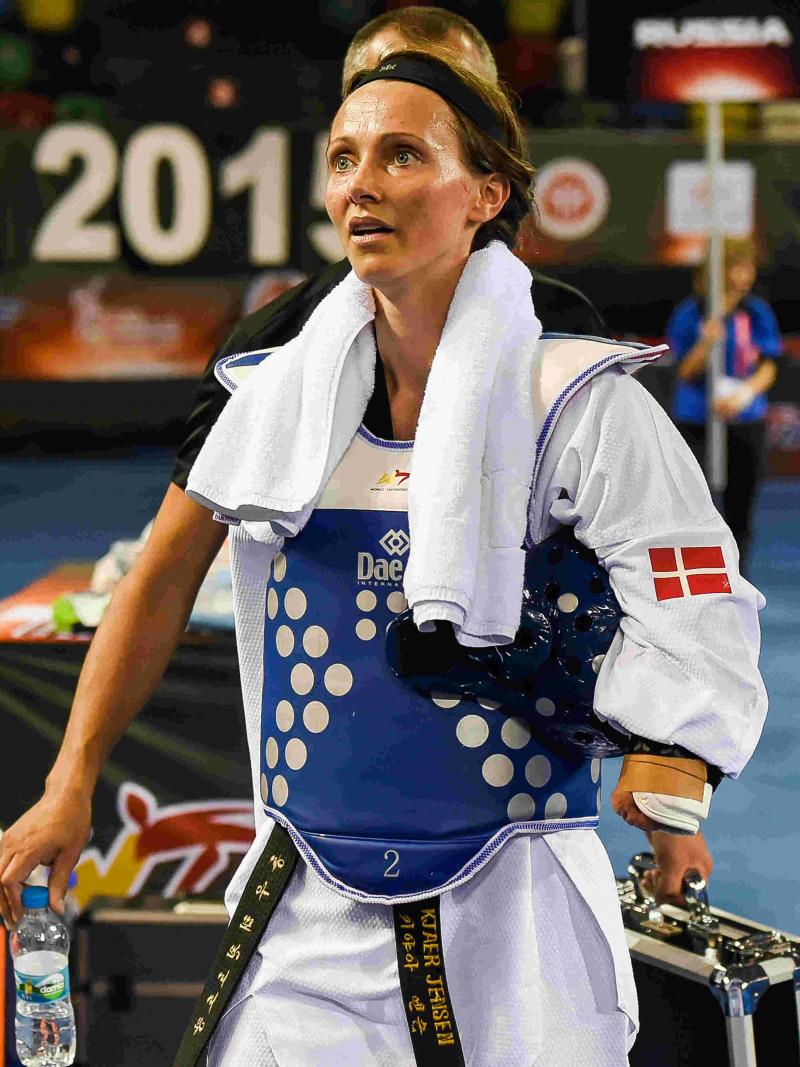 Female taekwondo athlete with right arm impairment walks off away from matt