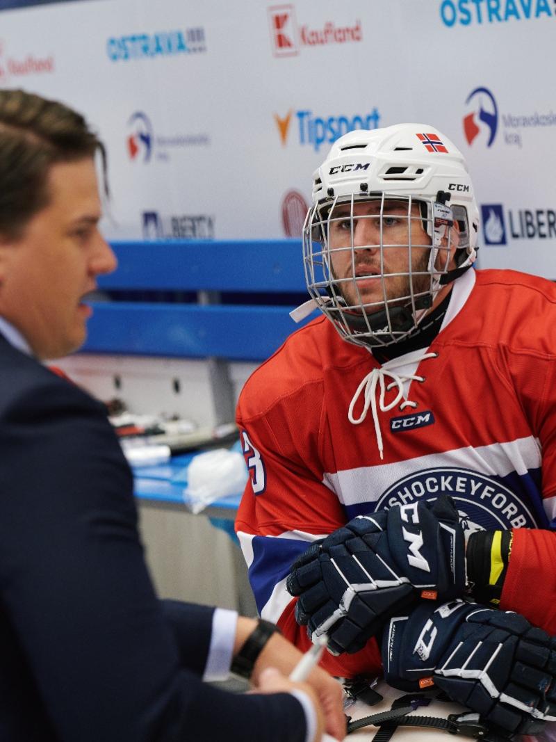 A man in a Para ice hockey uniform talking to another man in a suit in a Para ice hockey game