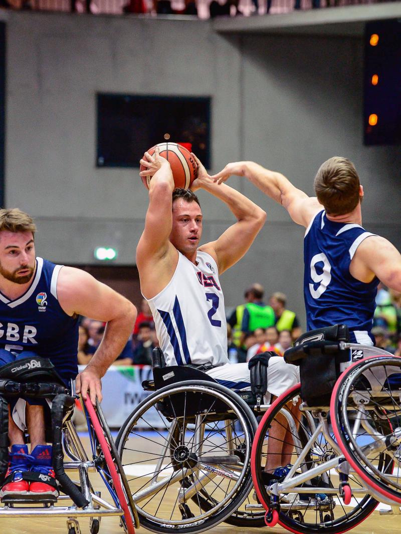 US wheelchair basketball player Jake Williams holds the ball on top of his head preventing British defenders from taking posession of it