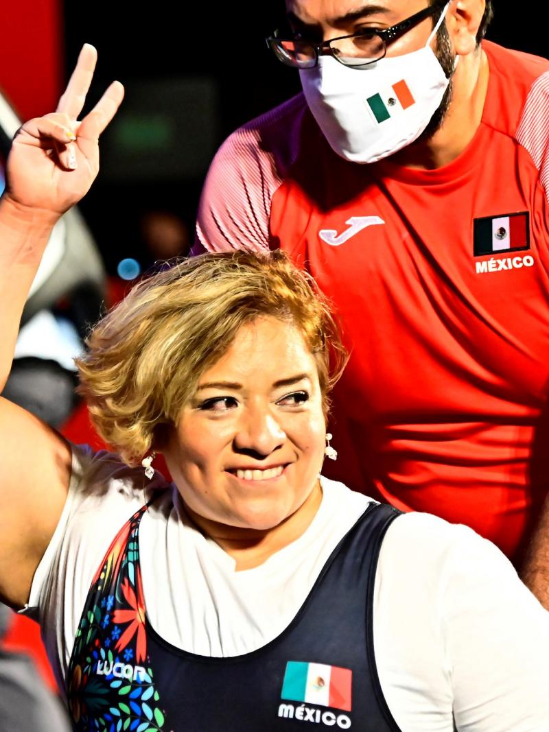 A woman smiling and raising her arm in a wheelchair chair being pushed by a man
