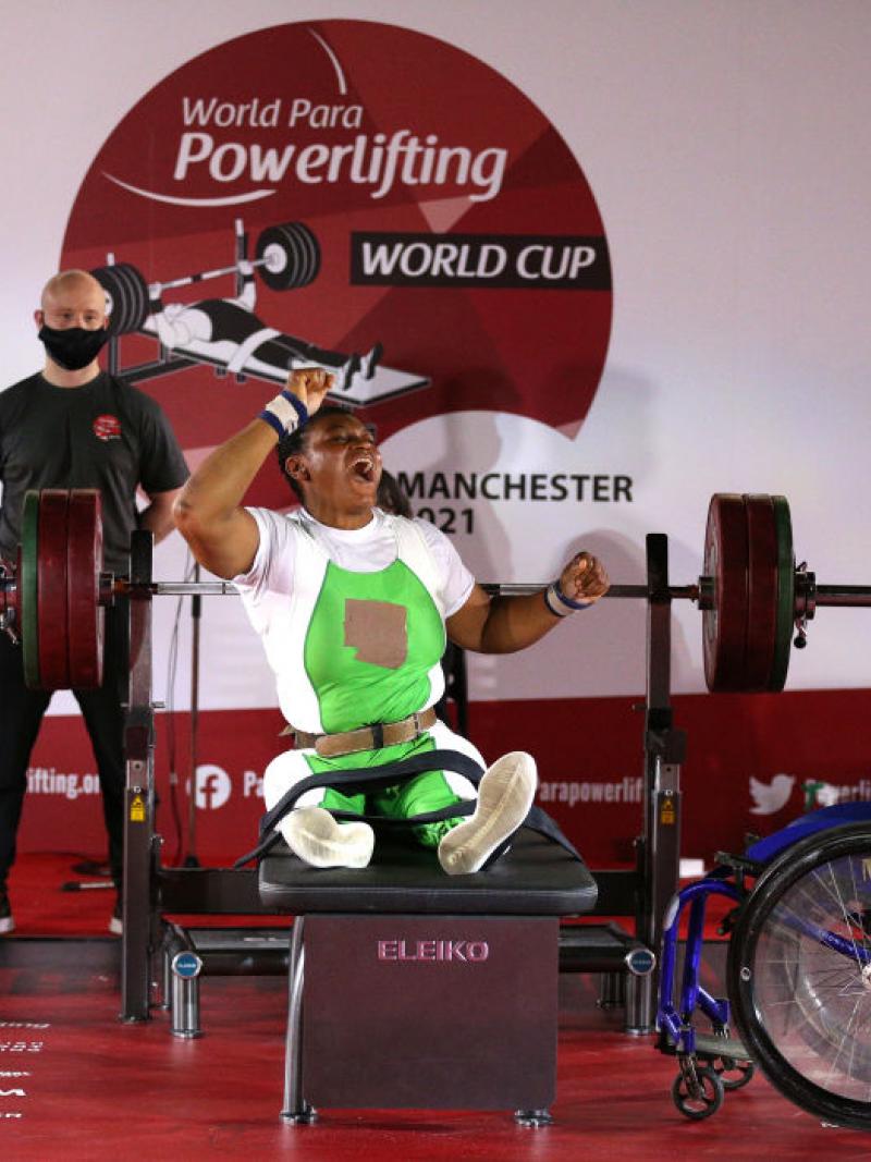 A woman celebrating on a bench press during a Para powerlifting event with four male loaders standing near her