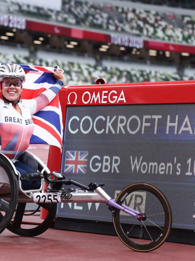 A woman in a racing wheelchair holding a British flag next to a board with her name and world record