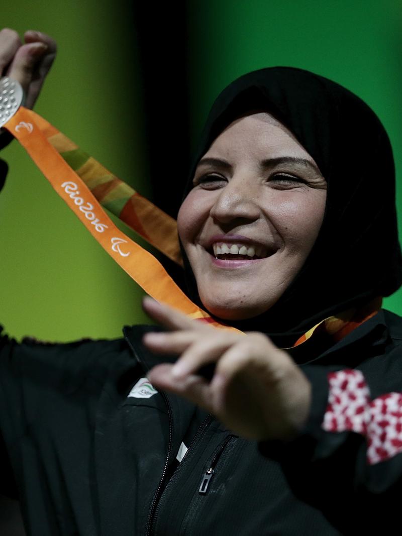A woman with a veil smiling and showing her medal