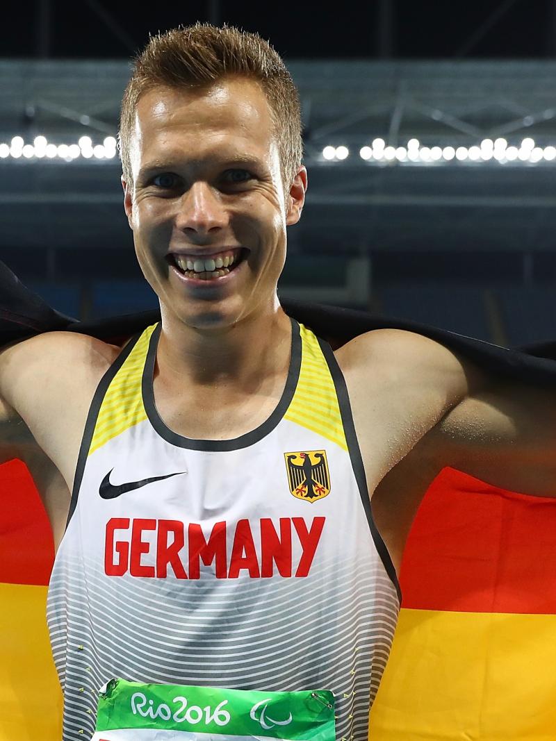 An smiley athlete holding the German flag behind his back