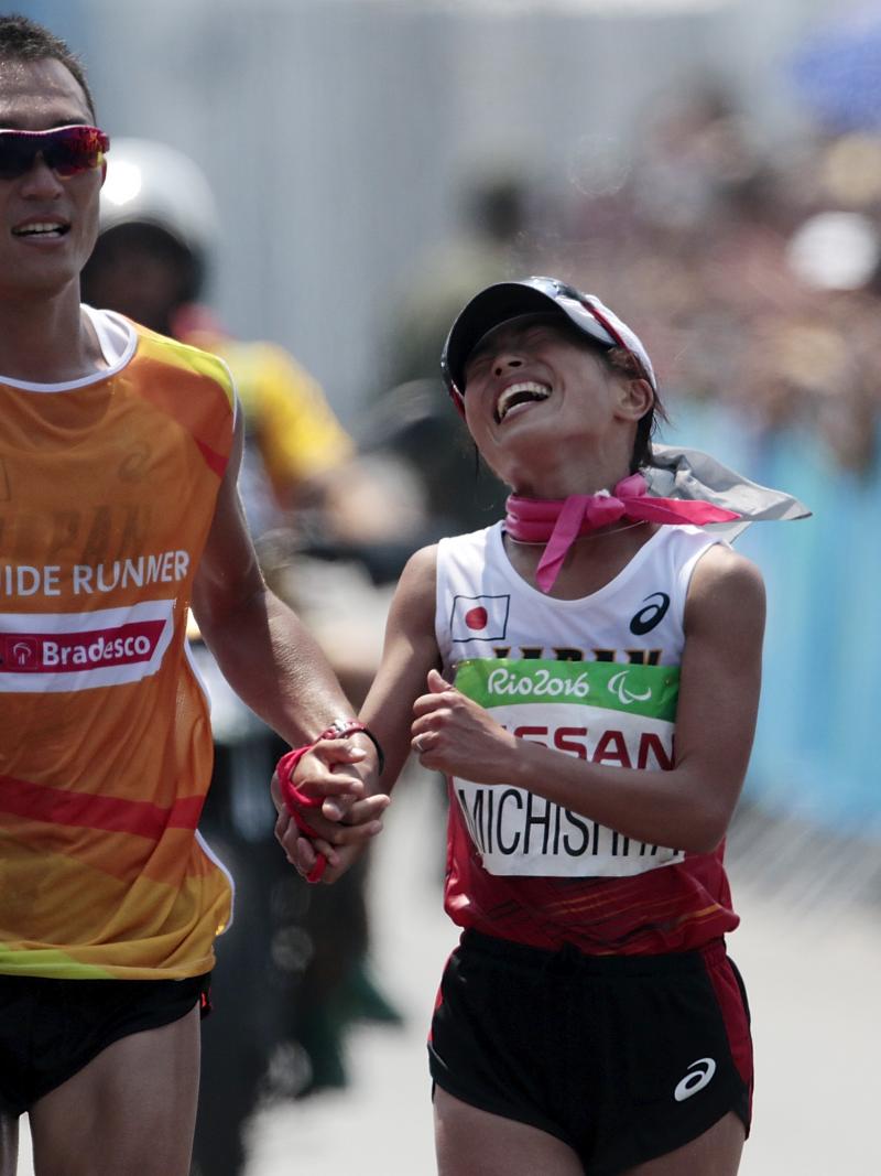 A woman running right next to a male runner guide during a marathon on a street