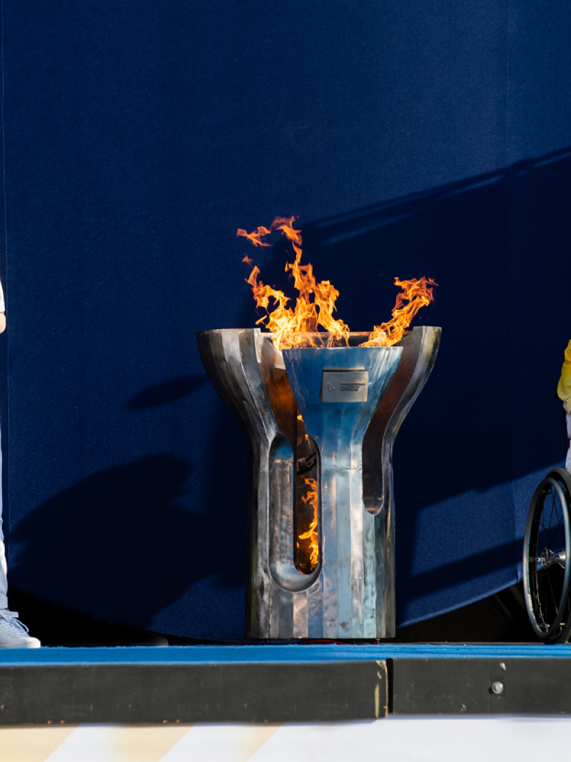 Two people holding torches with the Paralympic cauldron and flame in between