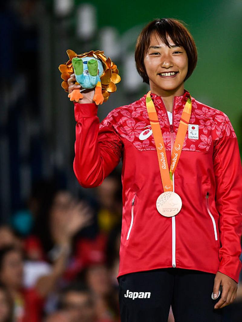 Japanese female judoka smiles on podium holding Paralympic mascot gift