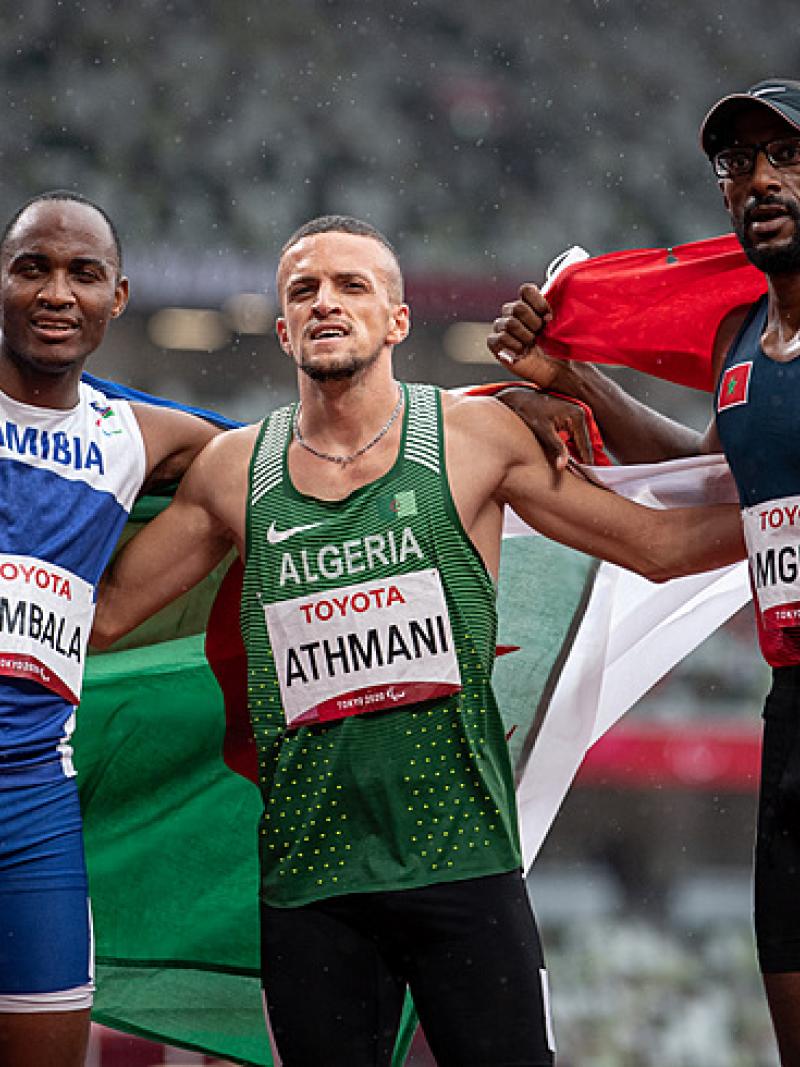Three men on an athletics track with their flags 