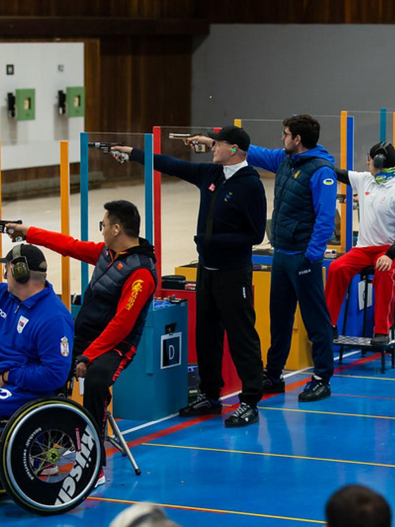 A group of eight men competing in a pistol shooting event in a shooting range