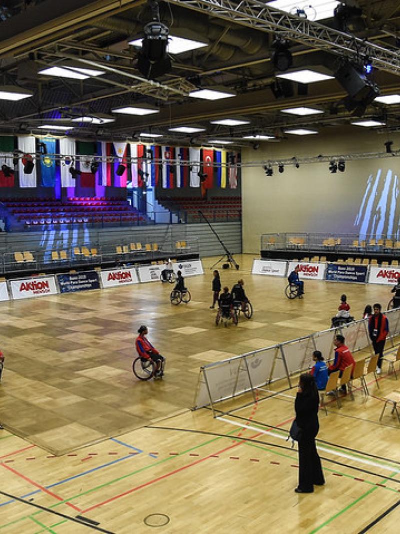 An indoor court with a group of Para dancers practicing observed by a group of people around the court