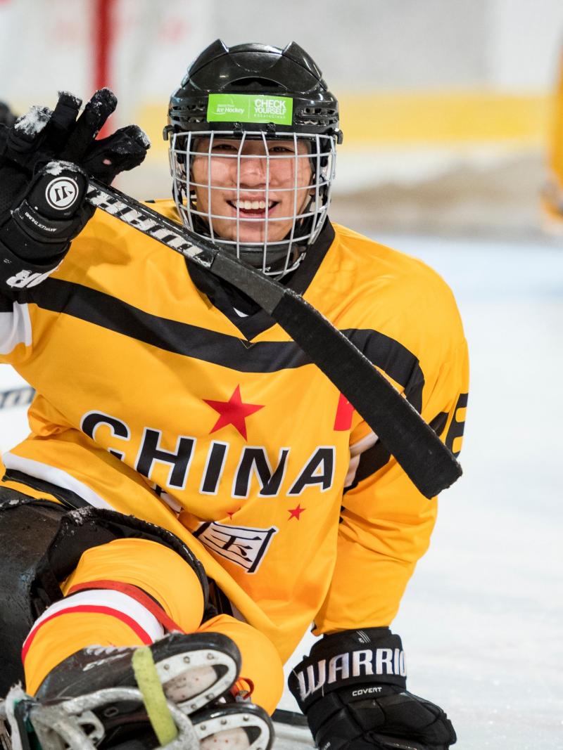 A Para ice hockey player celebrates scoring a goal with a smile on his face