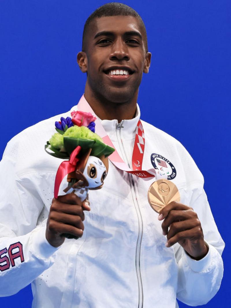 A man with the uniform of USA on a podium holding his medal 