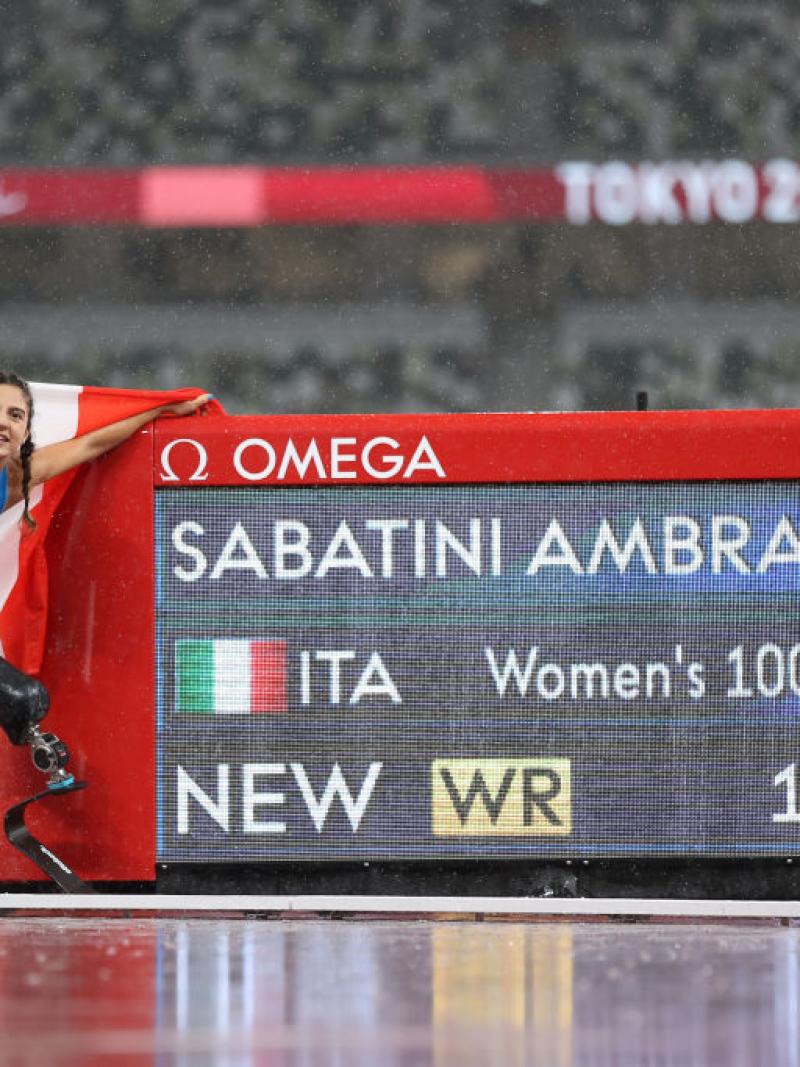 A woman with a prosthetic leg standing next to a screen showing her name and record on an athletics track