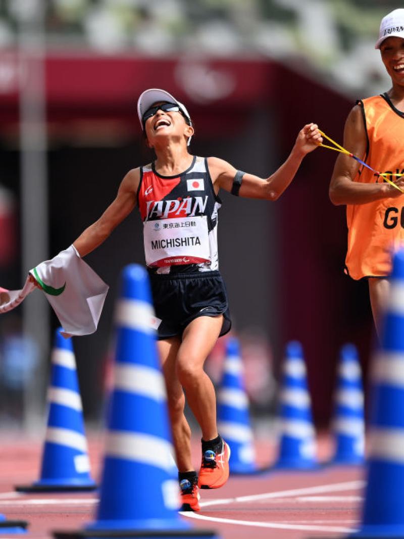 A female runner and her guide crossing the finish line in an athletics stadium