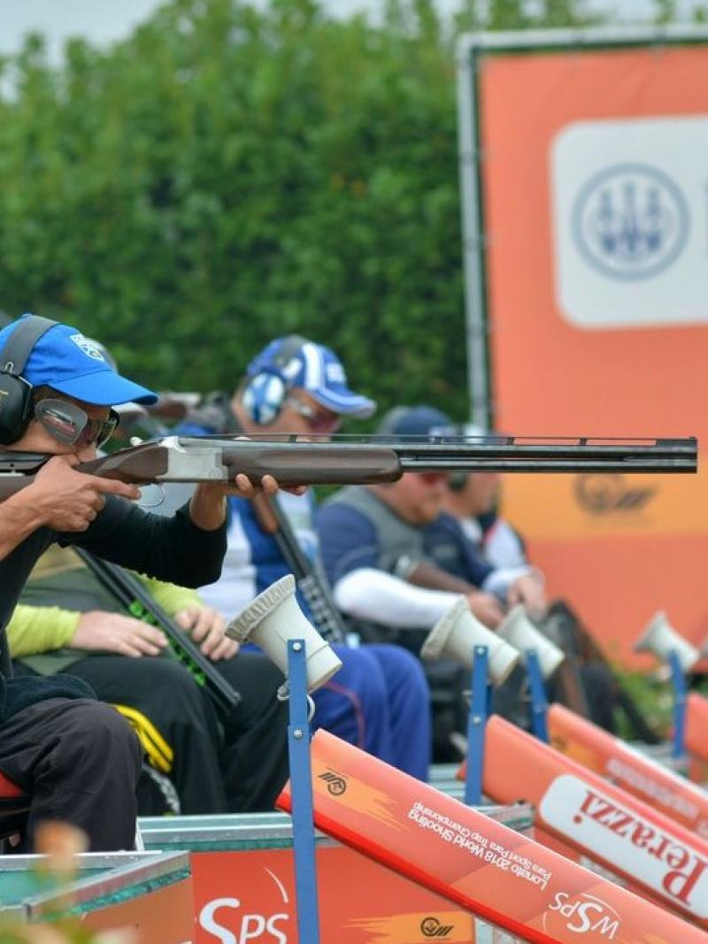 A man in a wheelchair competing with a shotgun in a Para trap event observed by other four competitors