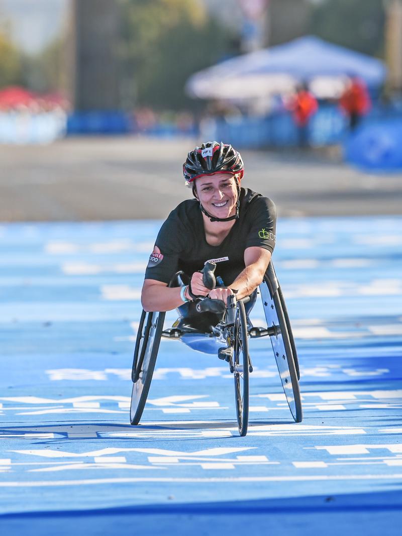 A female wheelchair racer smiling crossing the finish line on a street race