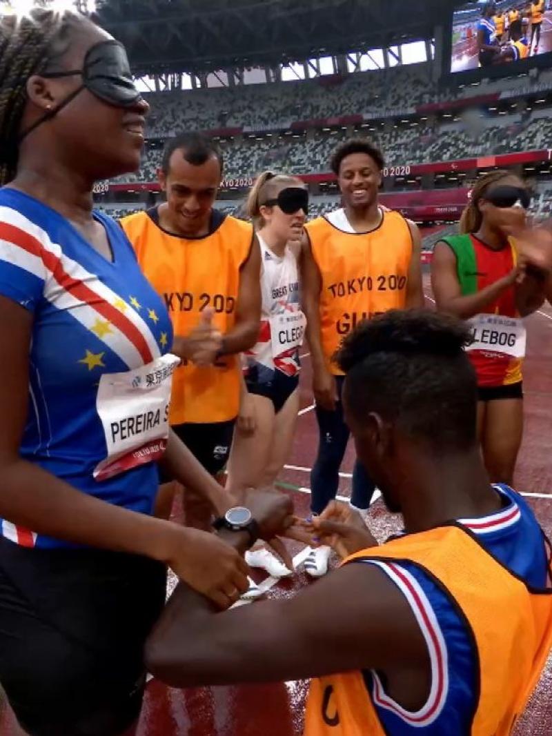 A man kneeling on an athletics track to propose a female athlete surrounded by four people