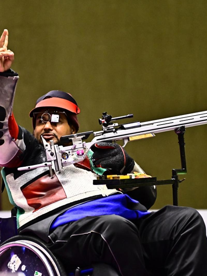 A man in a wheelchair waving in a shooting competition with a rifle