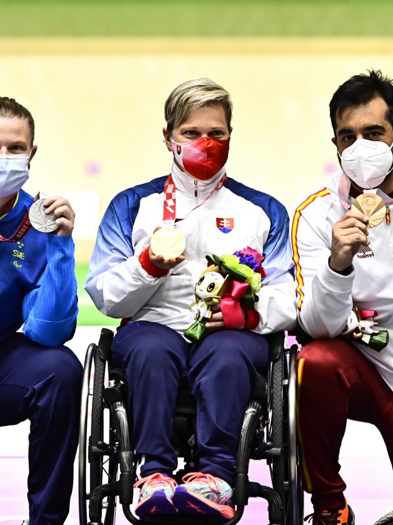 A woman and a man kneeling with their medals around a woman in a wheelchair showing her medal