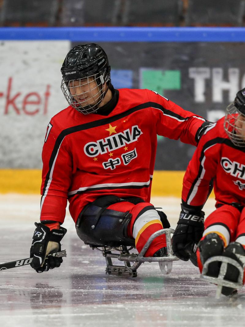 Chinese Para ice hockey player skating on a sled while controlling the puck with his right stick