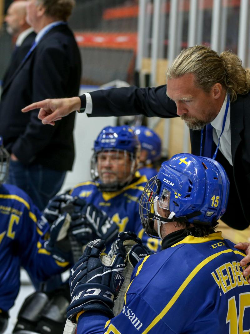 A man talking to Para ice hockey players on sleds pointing finger to the ice