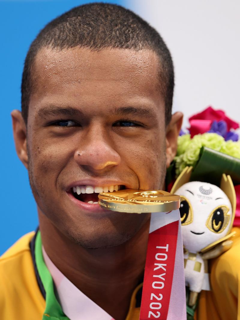 A man poses for photos biting a gold medal