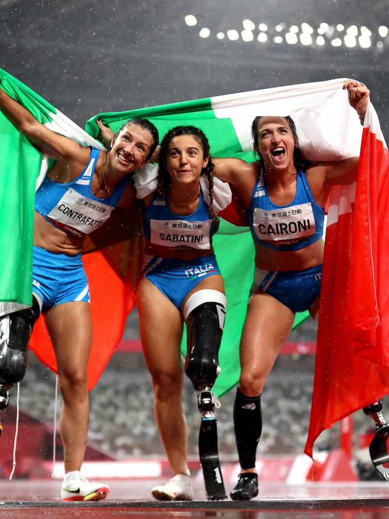 Three female athletes posing for a photo with flags while the rain is falling