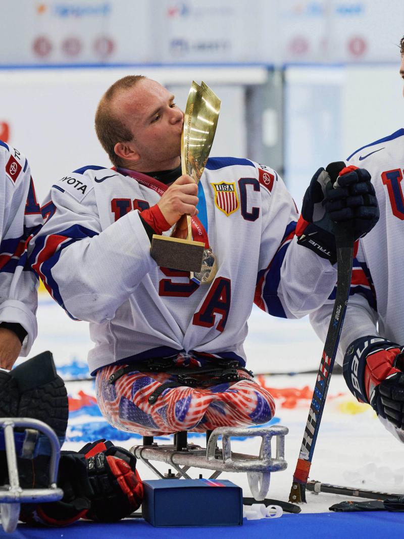 A Para ice hockey player kissing a trophy with the fireworks behind him