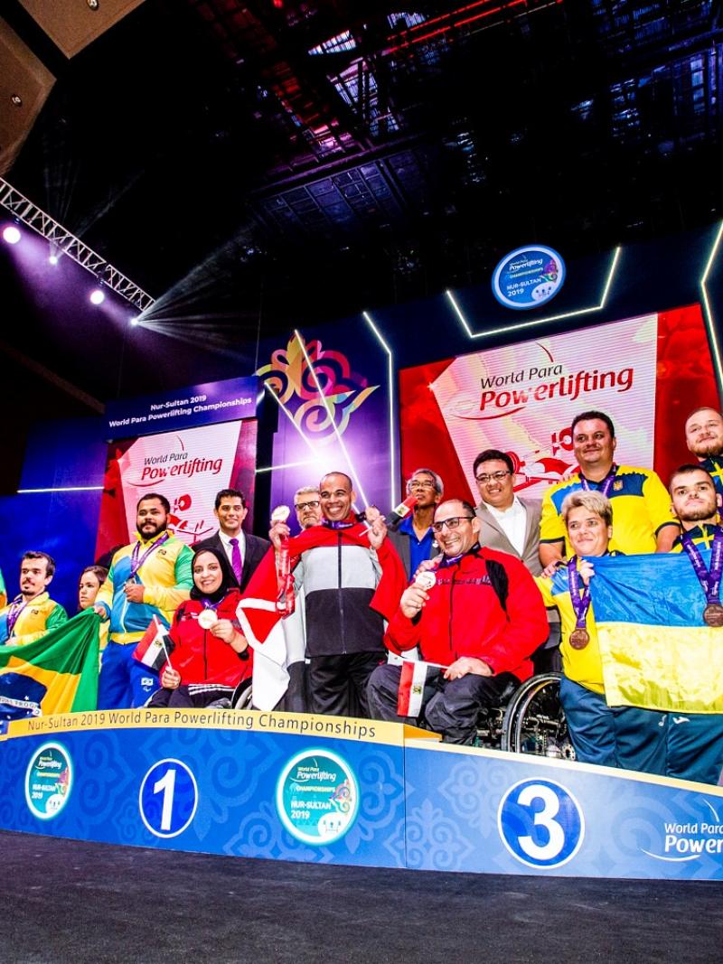 Athletes on the podium with team representatives posing for a photo with flags.