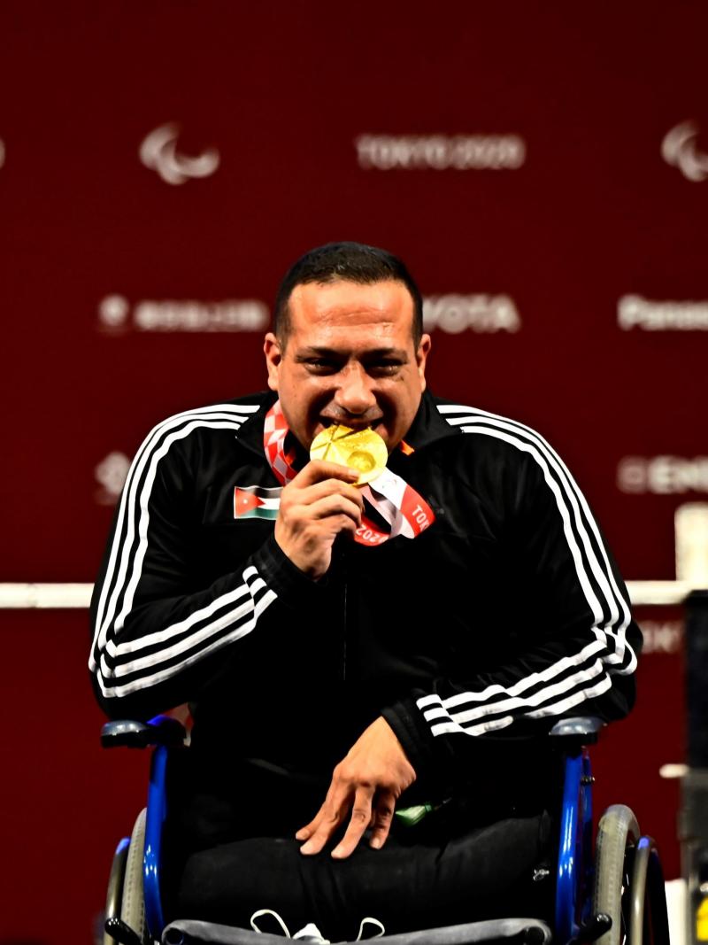 A man in a wheelchair biting the gold medal with a smile on his face