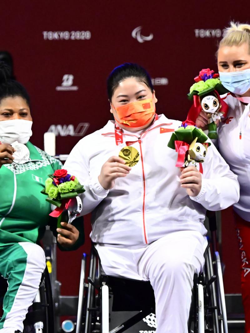 Three female athletes posing for a photo on the podium with medals around their necks.