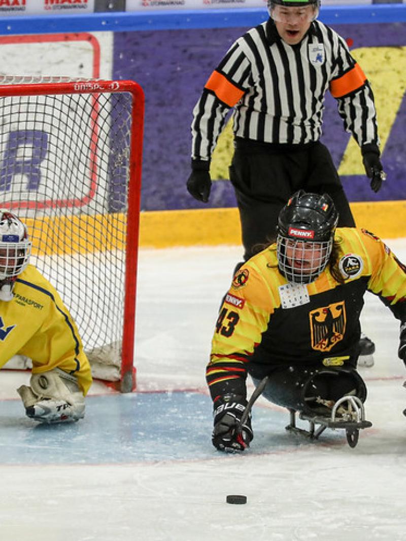 A German Para ice hockey player on ice competing against three Swedish players observed by a referee