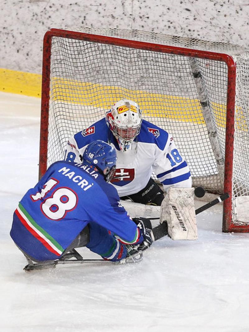 A Para ice hockey player hitting the puck in front of the goaltender