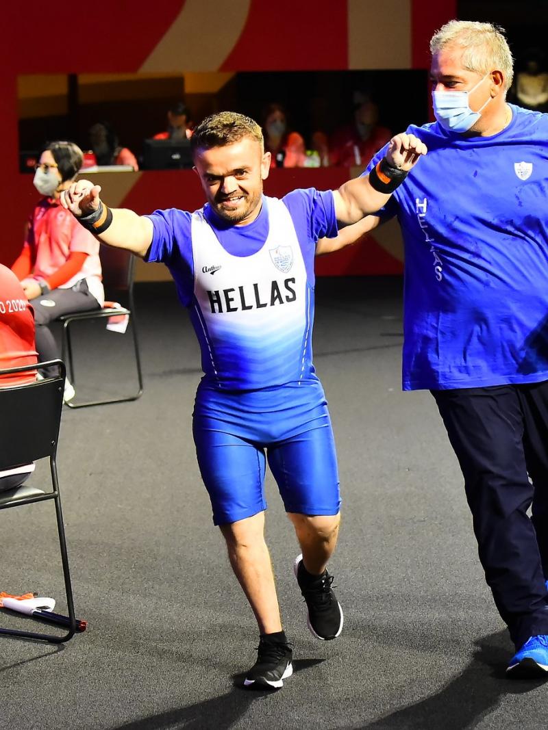 A man walking with his arms raised and a smile on his face while his coach taps him on the back.