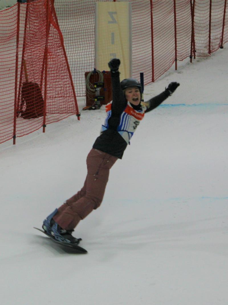 A female Para snowboarder stretching her arms in celebration in an indoor snow slope