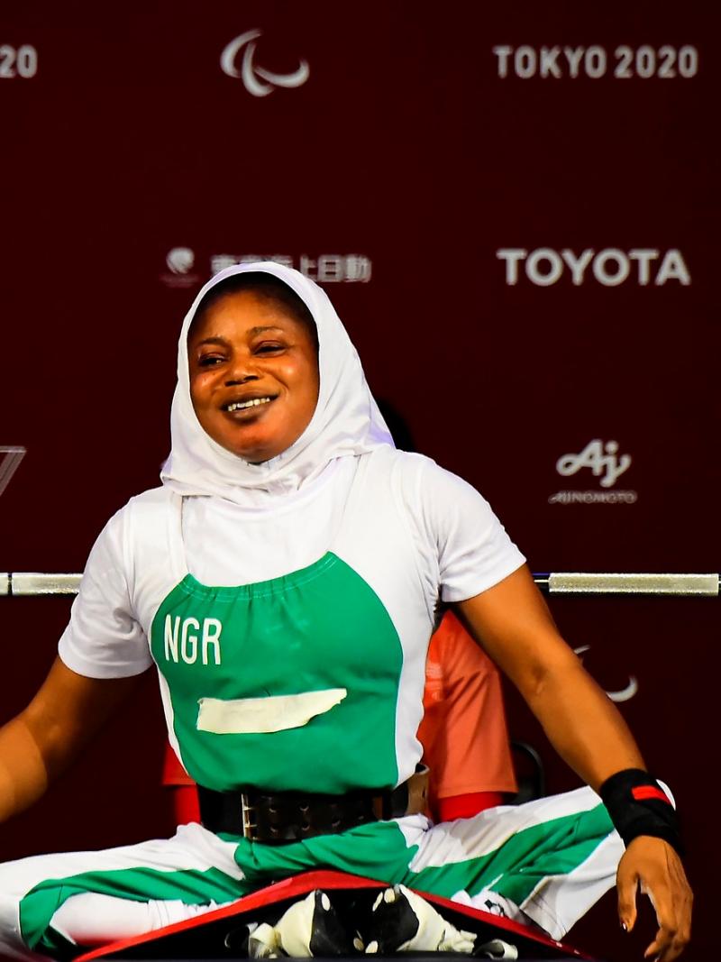 A woman sitting on the bench with her legs crossed and a smile on her face.