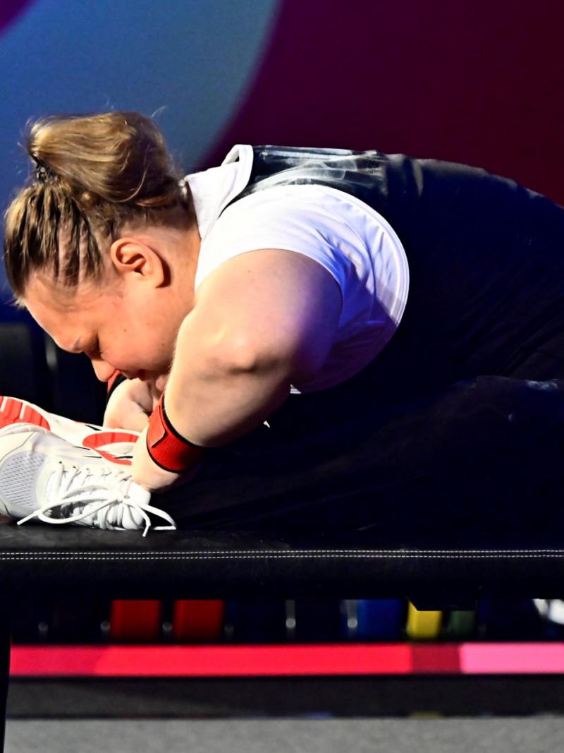 A female athlete stretching on the bench before her attempt.