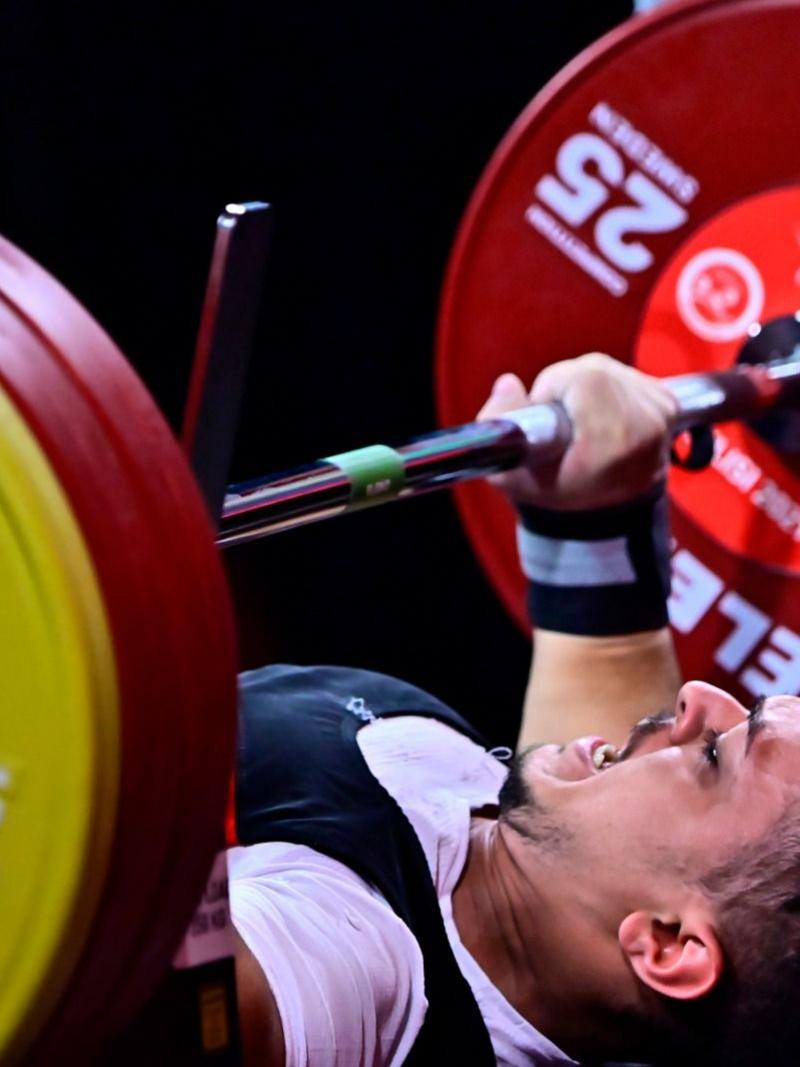 A young man lifting a bar in a Para powerlifting competition