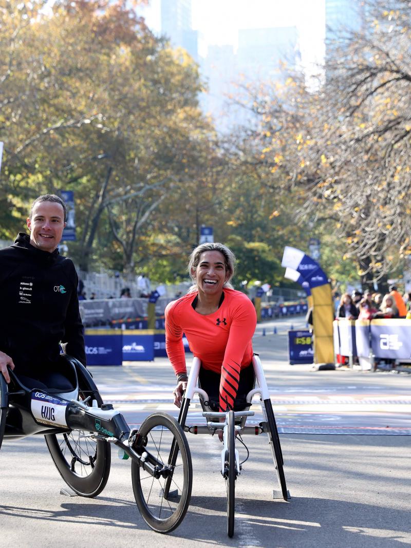 A man and a woman in wheelchair posing for a photo in front of the marathon finish line