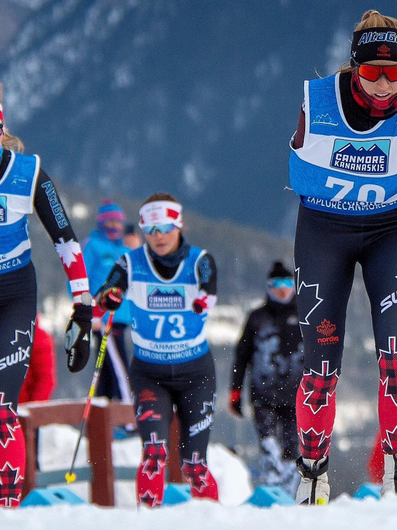 Three standing skiers climbing up the hill on a snowy road