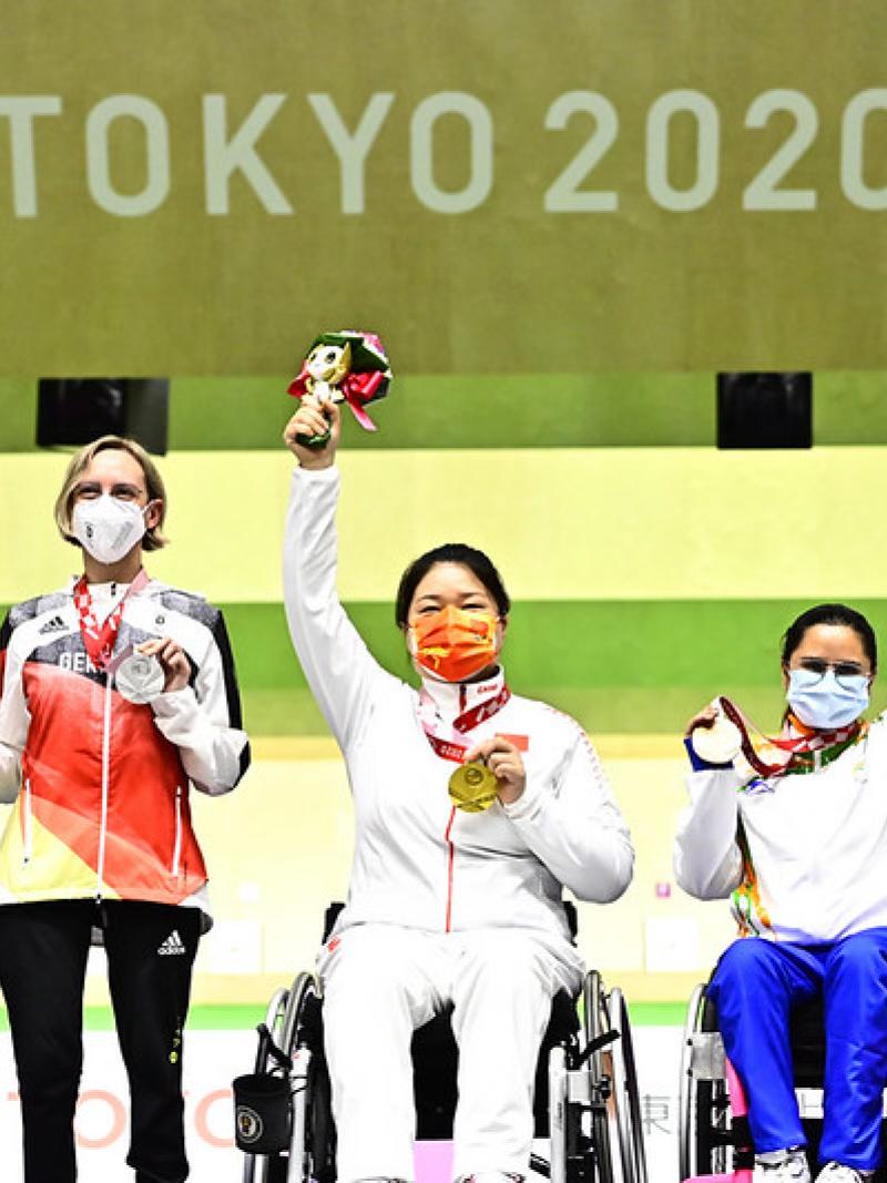 A woman standing next to two female wheelchair users on a podium at Tokyo 2020