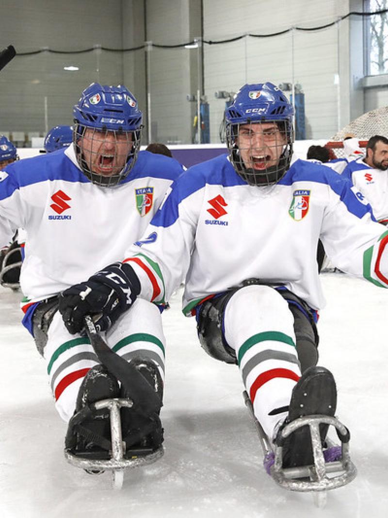 Two Italian Para ice hockey players celebrating with their team in the background in an ice rink