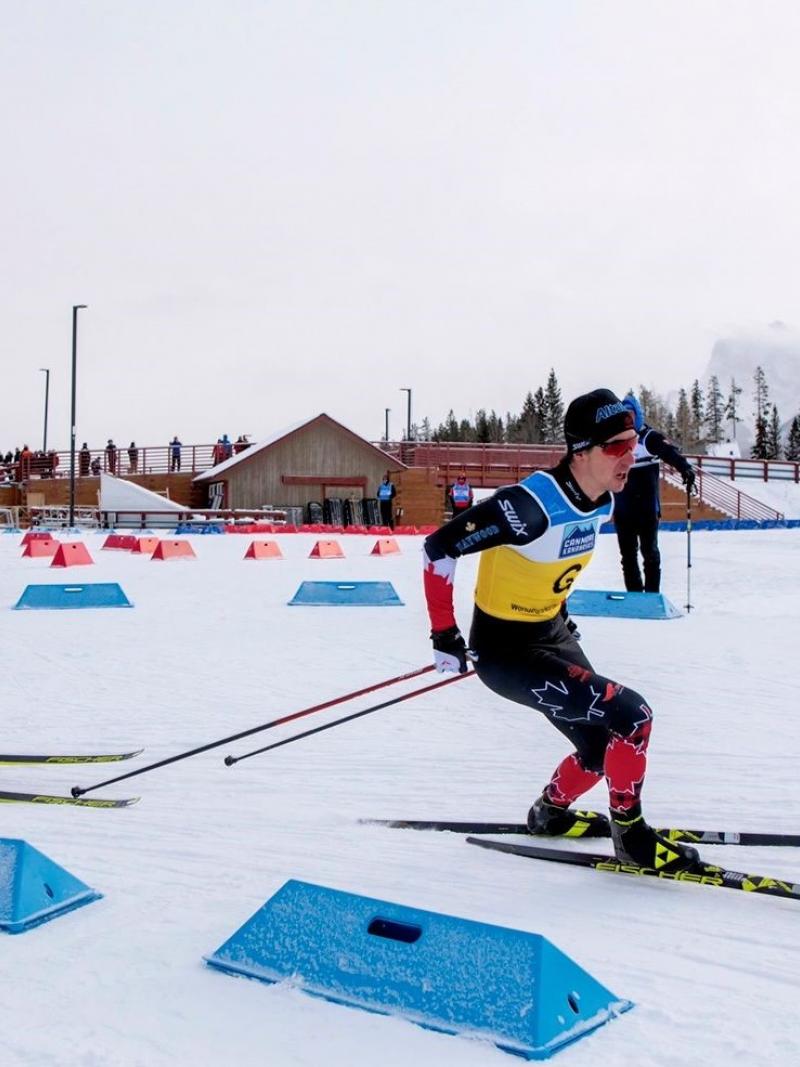 A male cross-country skier following his guide on a snowy track observed by three people