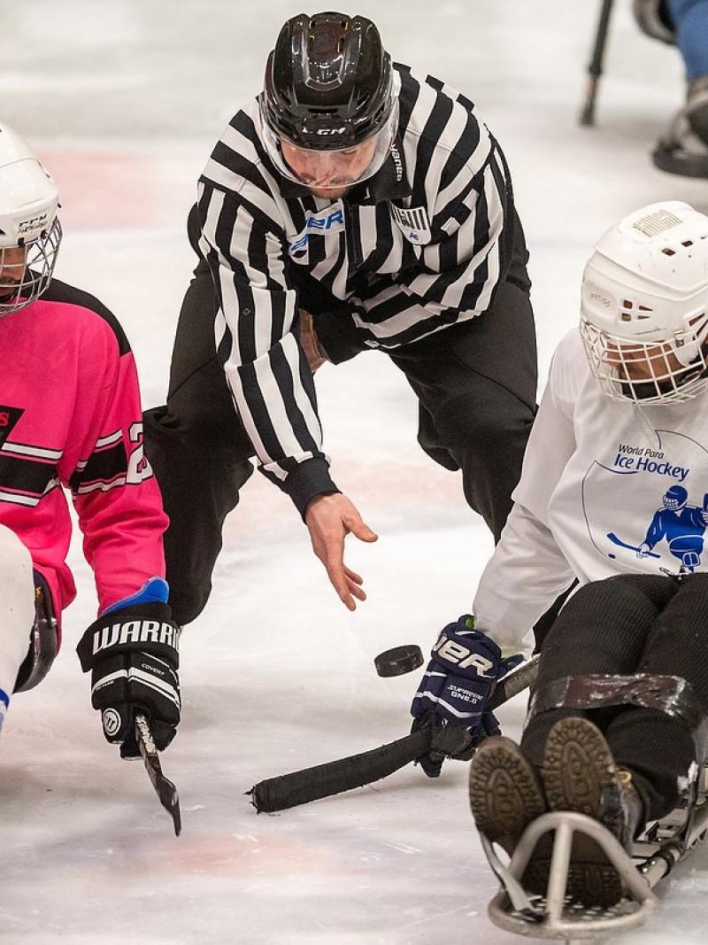 Two Para ice hockey players with a referee in the middle
