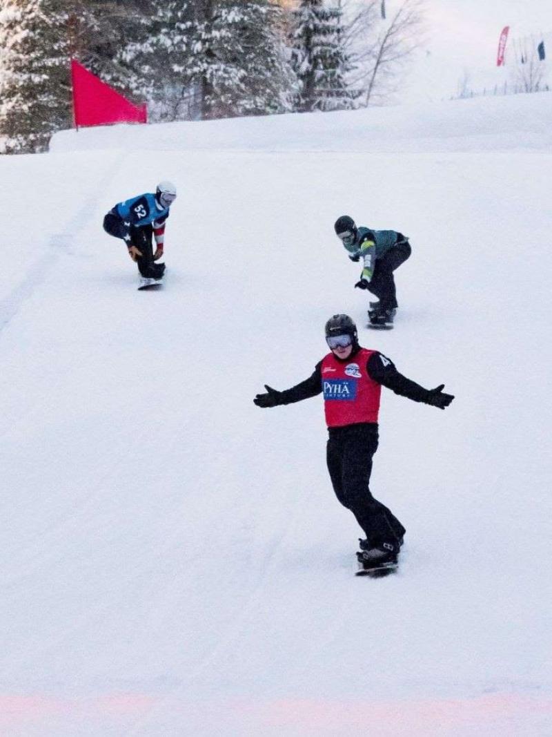 A male Para snowboarder crossing the finish line ahead of other two athletes