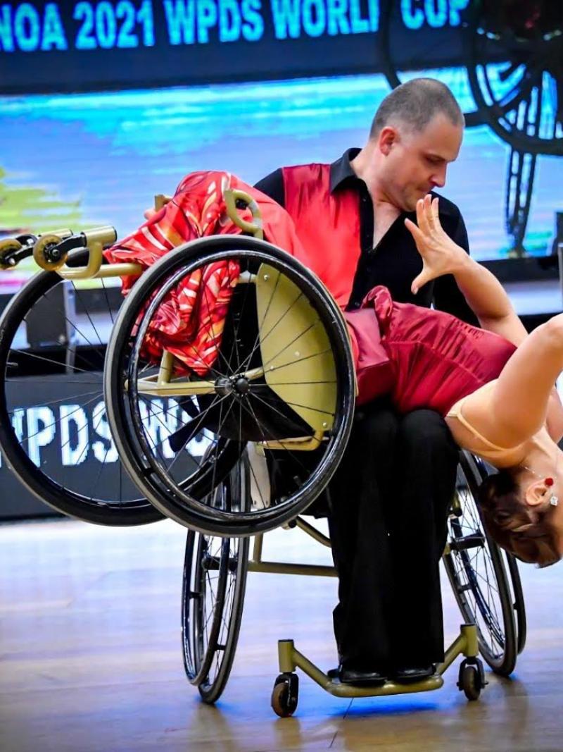 A male wheelchair dancer holding a female wheelchair dancer on his lap
