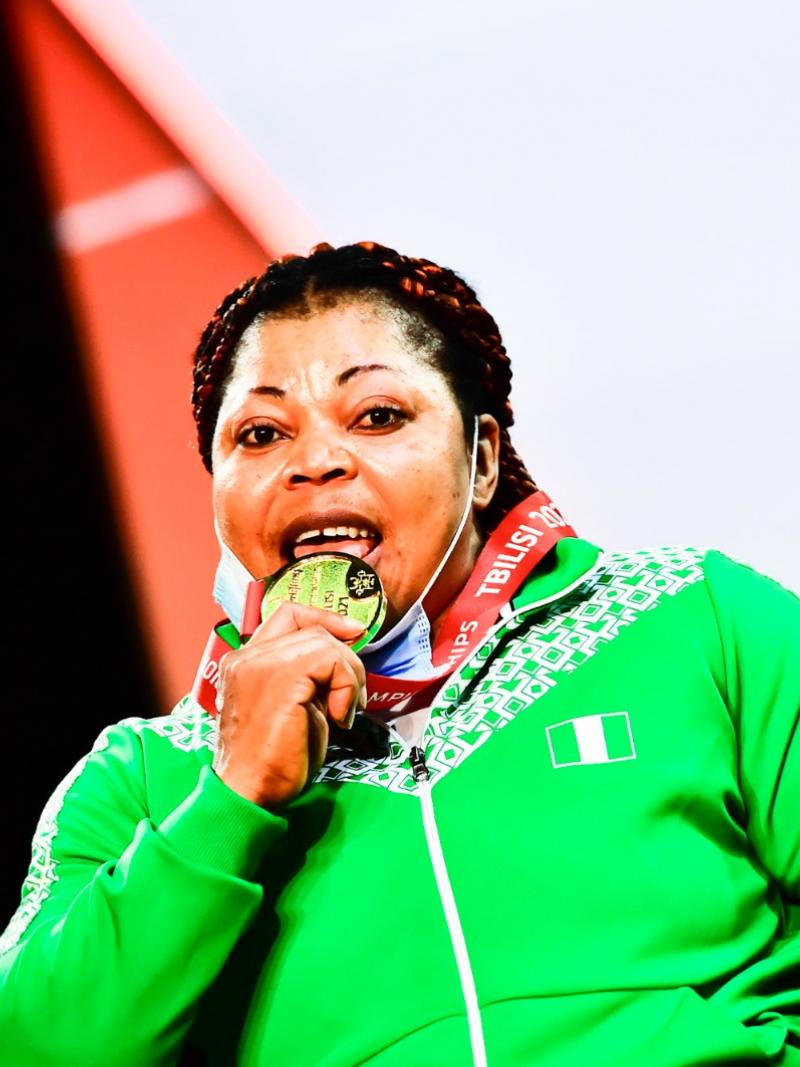 A woman in green uniform biting her gold medal
