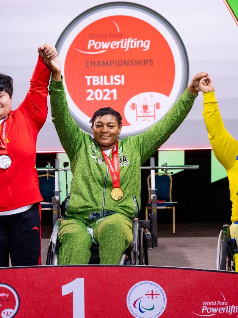 A woman in a wheelchair holding arms with a standing woman and another woman in a wheelchair in a podium