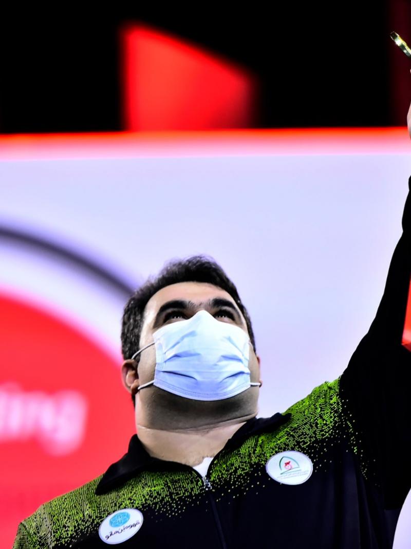 A man holding a gold medal and looking at the sky 
