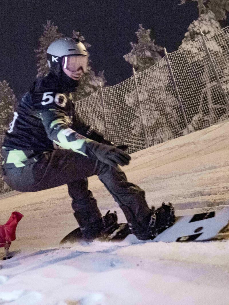 An athlete snowboarding during the night with goggles and helmet.